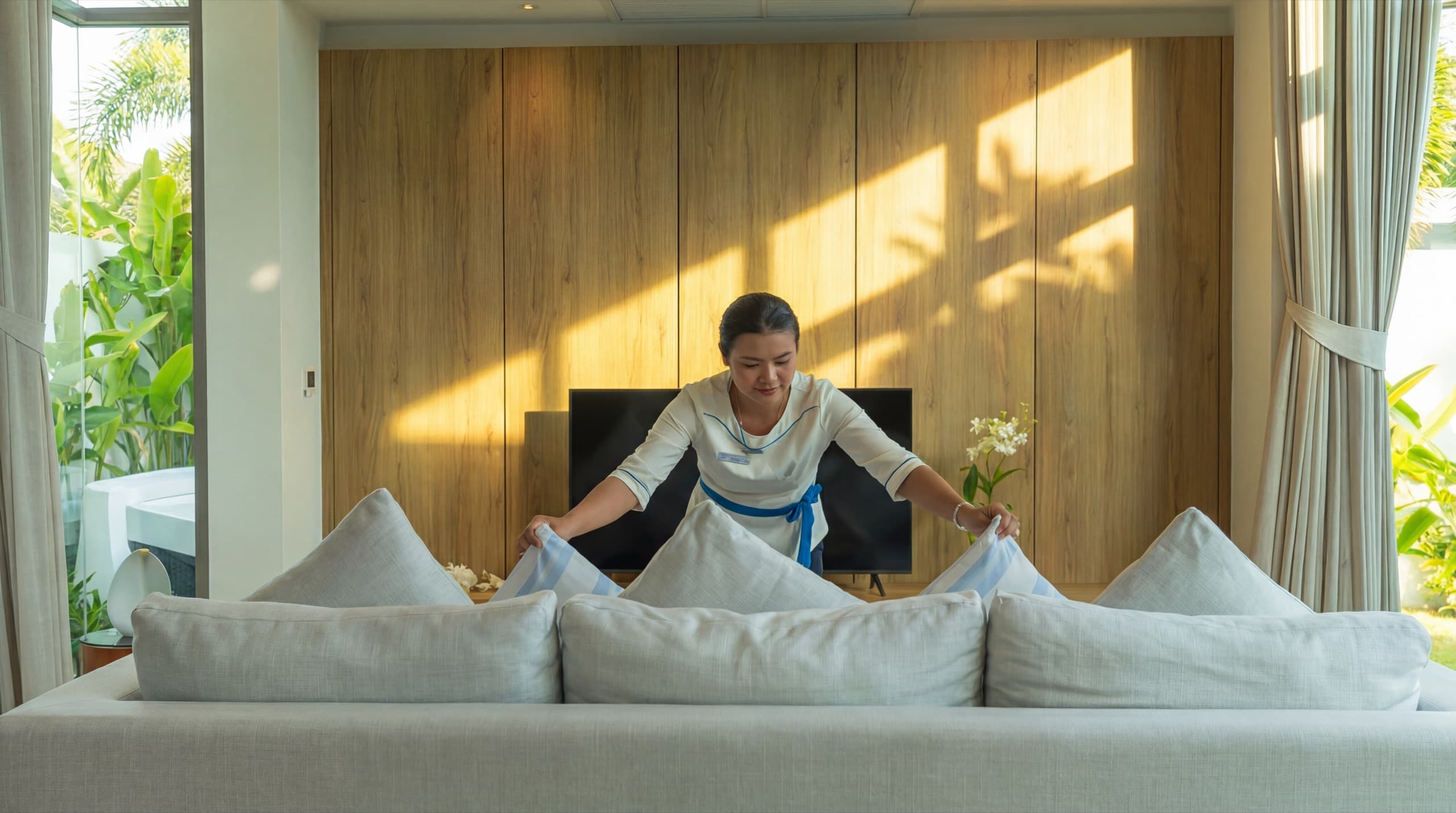 An Escape Villas housekeeper styling the living-room sofa in a sunlit villa to a five-star standard